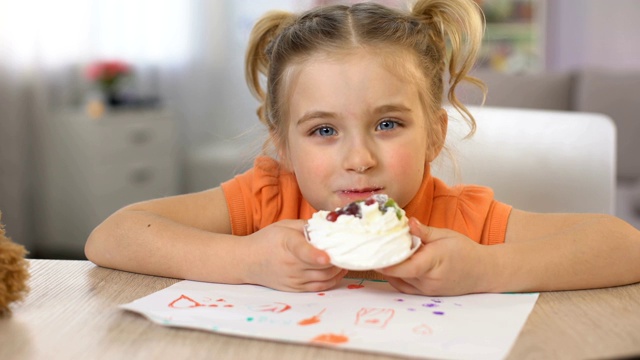 可爱的小女孩坐在桌子上吃着甜甜的奶油蛋糕，童年幸福视频素材