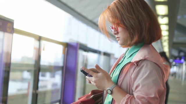 一名女子在火车站站台上使用智能手机，慢镜头视频素材