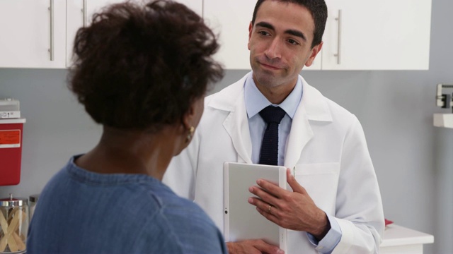 迷人的年轻西班牙裔医生使用平板电脑查看病人的医疗档案视频素材