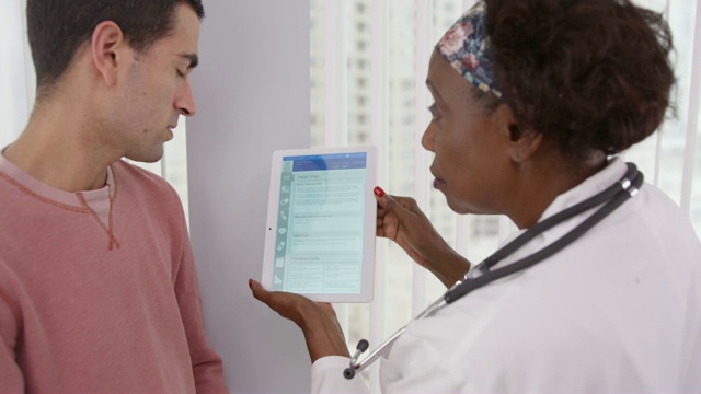 高级非洲医学博士向男性拉丁裔患者展示平板电脑上不同的健康计划视频下载