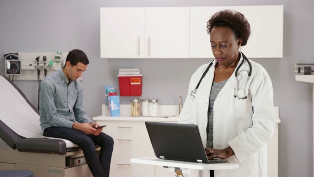 高级黑人医生在便携式电脑上记录单个拉丁裔病人视频素材