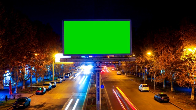 一个广告牌与绿色色度键在一个城市夜间景观快速移动汽车与长曝光的背景。时间流逝的视频。摄影机过来了。视频下载