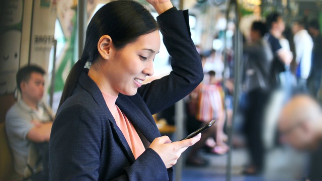 年轻的亚洲女性在公共交通上使用智能手机，在地铁上使用社交媒体女性上网视频素材