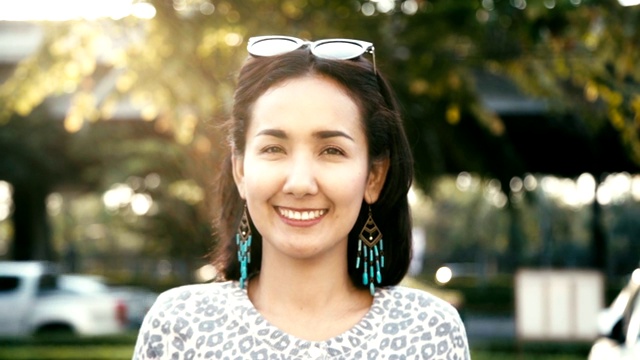 年轻美丽的亚洲女人的肖像快乐和微笑看起来友好的户外相机。缓慢的运动。视频素材