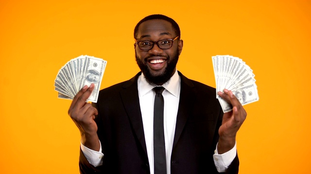 戴着眼镜的黑人男性展示着一堆现金，利润，利润丰厚的生意视频素材