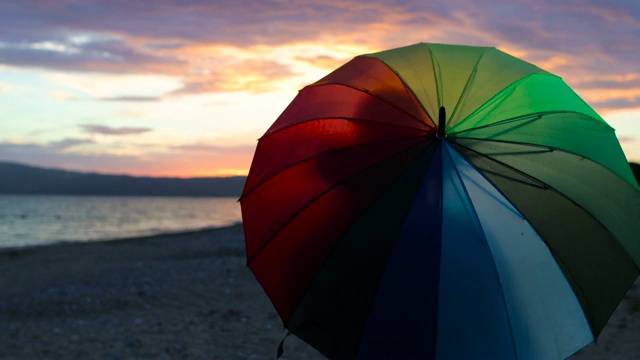 日落时分，在沙滩上旋转彩虹伞的女子视频下载