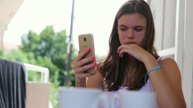 年轻的女孩看着她的手机前摄像头，她为她的痤疮问题感到难过视频素材