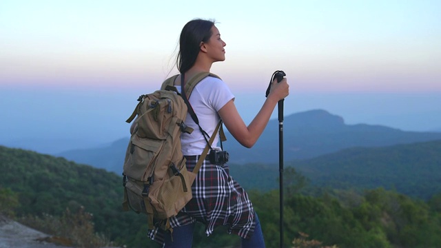 一位年轻的女游客正在山顶徒步旅行，观赏美丽的风景。视频素材
