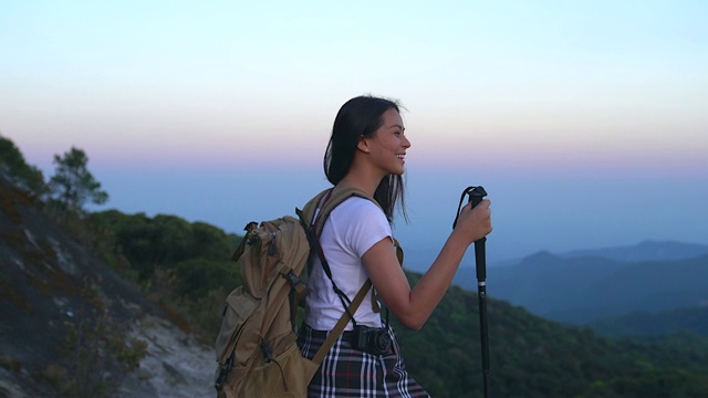 一位年轻的女游客正在山顶徒步旅行，观赏美丽的风景。视频素材