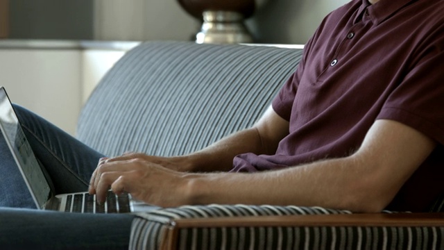 微笑的男性影响者在家里的沙发上使用笔记本电脑视频素材