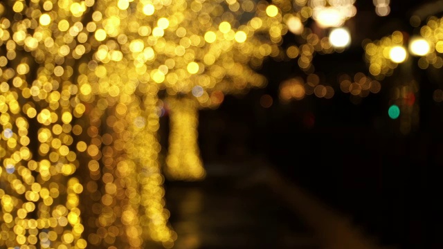 树上的金色花环在街道上模糊不清。圣诞节和新年假期的背景。模糊散景花环视频素材