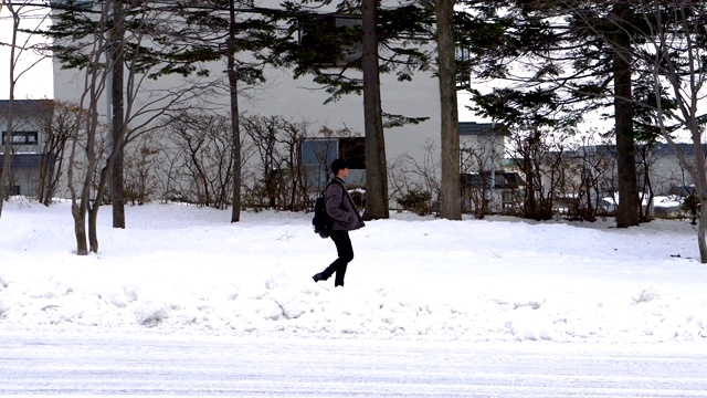 侧视图-在郊区的冬天，一个人走在被雪覆盖的人行道上视频素材