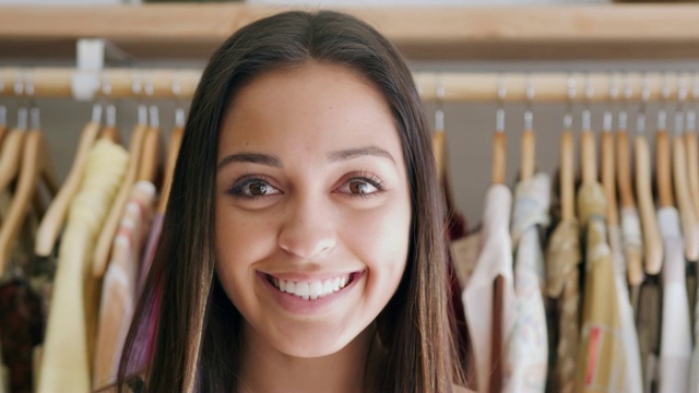 一个微笑的年轻女人的肖像站在时装店的衣架衣服-拍摄的慢动作视频素材