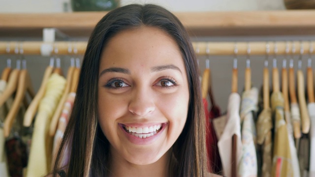一个微笑的年轻女人的肖像站在时装店的衣架衣服-拍摄的慢动作视频素材
