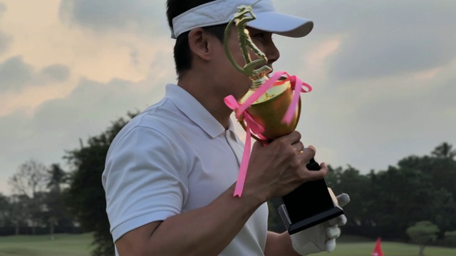 快乐的高尔夫球手拿着司机和奖杯，同时举起他的手臂与日落的背景。成功的概念。体育cinemagraph视频素材
