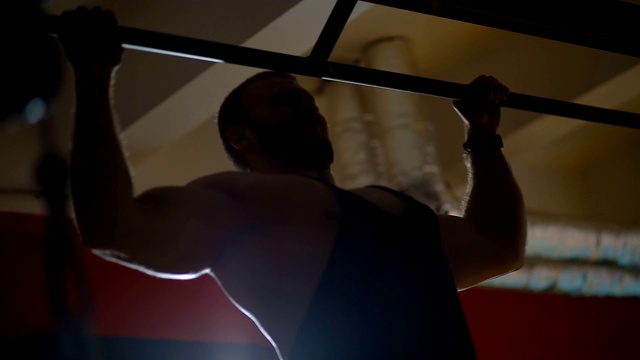 运动员在黑暗的体育馆背光下做引体向上视频素材