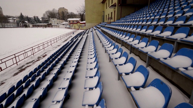 在冬季，体育场看台上一排排被雪覆盖的蓝色塑料座位视频素材