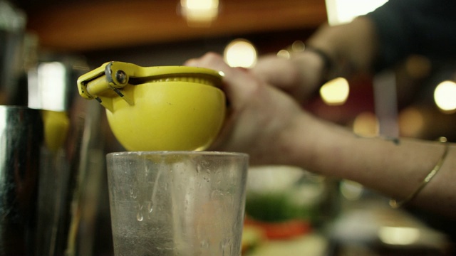 一个白人女调酒师使用柠檬挤压厨房工具挤柠檬汁到一个冰镇的透明玻璃，而在酒吧制作鸡尾酒视频下载