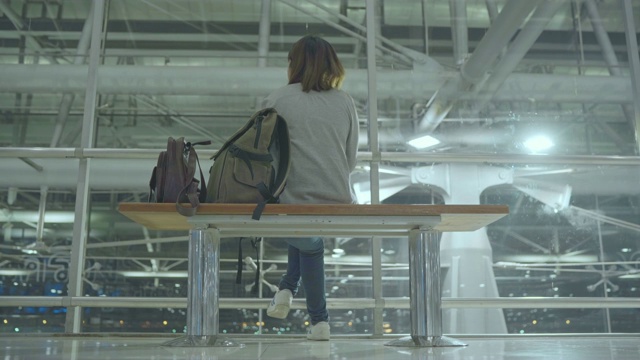快乐的亚洲女人坐在国际机场的椅子上环顾四周。视频素材