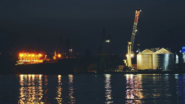 在明亮的落日背景下，在傍晚的海港卸货和装货。大型起重机在货船上装载散装货物视频素材