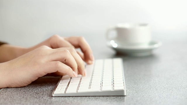 女性手的特写视频，在PS键盘上打字，在办公室的桌子上。视频素材