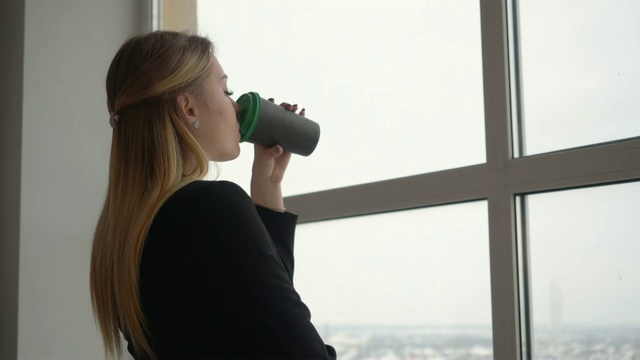 年轻的女设计师手里拿着咖啡杯在窗户背景上喝视频素材