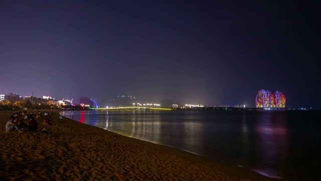 夜晚灯火辉煌的三亚拥挤的海滩著名的酒店全景4k时间推移海南岛中国视频素材