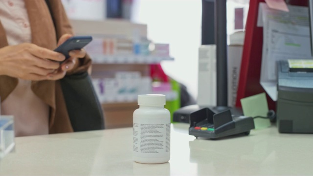 一位女士在药店用她的智能手机买了一瓶维生素视频下载