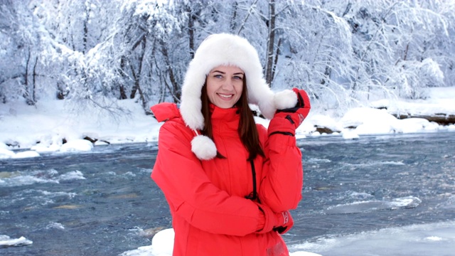 一个穿着红色夹克的女人在冬天的河边享受一个霜冻的早晨，把雪扔在自己身上，快乐地旋转着。视频下载