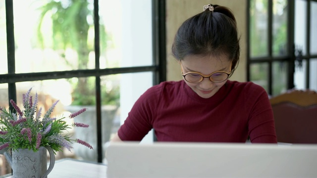 美丽的亚洲女人坐在笔记本电脑前在咖啡馆，看着相机和微笑。视频素材