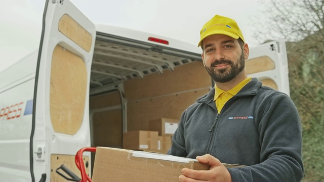 一个留着胡子的微笑男性快递员的肖像，他把包裹放在他的货车旁边视频下载