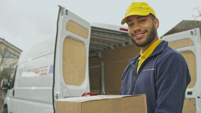 一个微笑的男快递员拿着一个包裹在他的货车旁的肖像视频下载