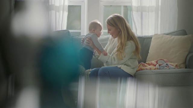 年轻的母亲在客厅的沙发上亲切地和婴儿说话。视频下载