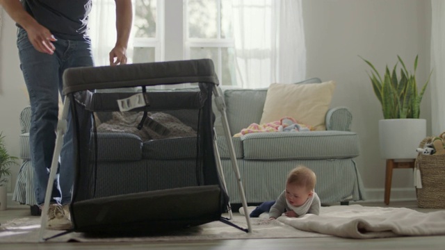 在客厅里，年轻的父亲收拾东西玩，可爱的宝宝在毯子上滚来滚去。视频素材