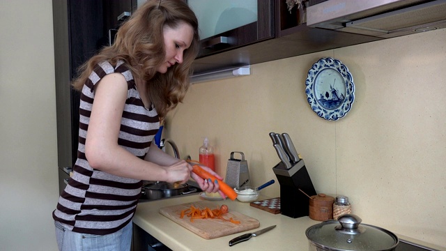 家庭主妇用削皮工具削橙胡萝卜皮。4 k视频素材