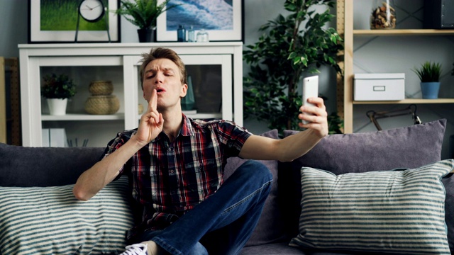 一名年轻人正坐在家里的沙发上用智能手机自拍视频下载