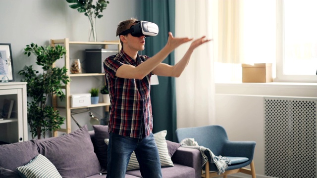 年轻人有虚拟现实眼镜站在家里和移动的手的经验。视频素材