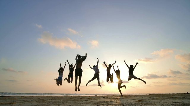 日落时分，朋友们在海滩上跳跃的剪影，心情愉快。4 k决议。慢动作镜头。视频下载