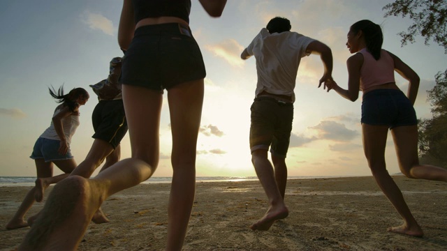 慢镜头-日落时分，一群朋友在海滩上奔跑，心情愉快。有聚会庆祝观念的人。后视图。视频素材