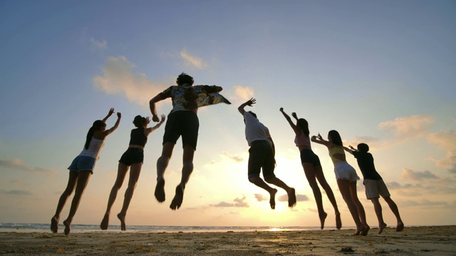 日落时分，朋友们在海滩上跳跃的剪影，心情愉快。4 k决议。慢动作镜头。视频素材