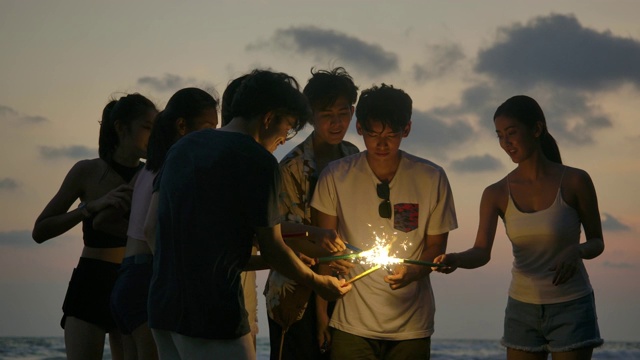 一群朋友在海边的夜晚聚会上玩的孟加拉灯在他们的手。青少年们在海滩上用烟花聚会。慢动作镜头。视频素材