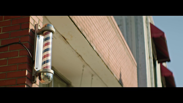 传统的红、白、蓝条纹理发店的电线杆开在小镇的一家砖瓦理发店外。视频下载