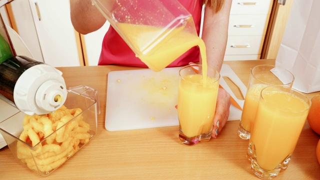 女子在榨汁机中制作橙汁，将饮料倒入4K玻璃杯中视频素材