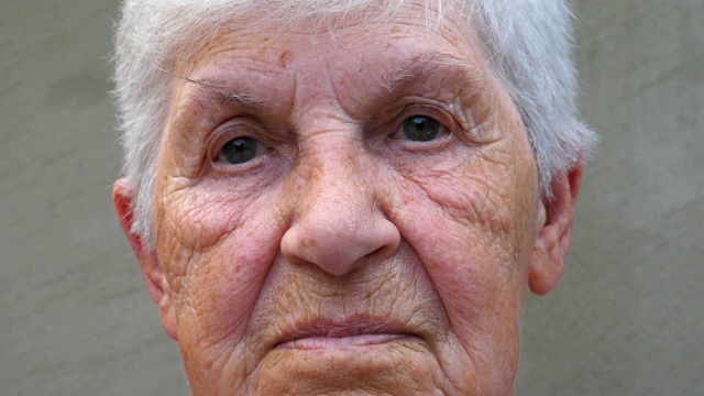 老祖母的肖像，带着悲伤的神情。满脸皱纹的老妇人看着镜头。老奶奶脸上悲伤的表情。近距离凝视成熟的女人。视频下载