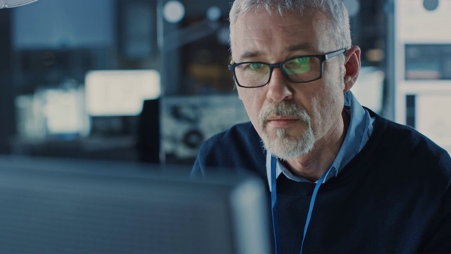 英俊的中年工程师戴着眼镜在个人电脑上工作的肖像。背景中的高科技工程设施视频素材