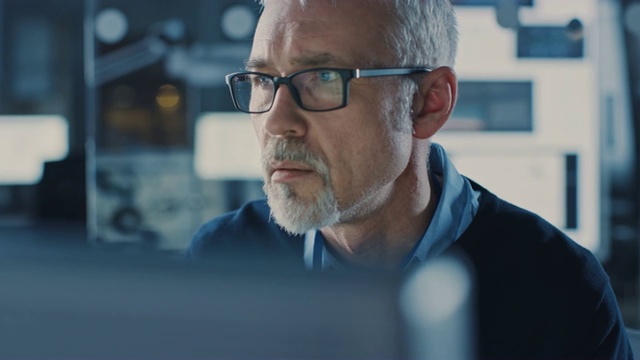英俊的中年工程师戴着眼镜在个人电脑上工作的肖像。背景中的高科技工程设施视频素材