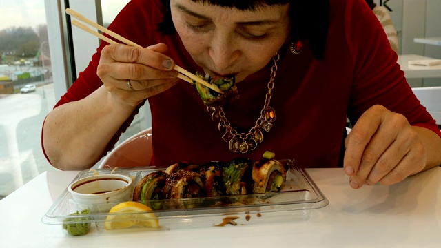 一名女子在餐馆里用木筷子吃寿司，配上芥末、生姜和酱油。视频素材