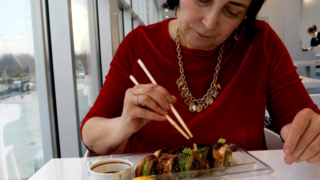 一名女子在餐馆里用木筷子吃寿司，配上芥末、生姜和酱油。视频素材