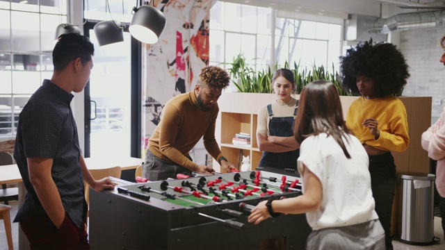 年轻的商业创意人士在工作中玩桌上足球来休息视频素材