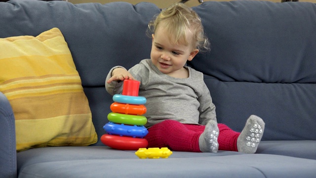 小女孩坐在沙发上玩金字塔塔。早期教育的概念。视频下载
